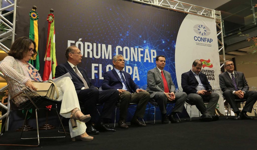 Sentados em frente a um painel escrito "Fórum Confap", quatro homens e uma mulher