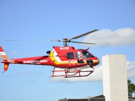 Helicóptero vermelho sobrevoa prédio com céu azul ao fundo