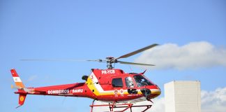 Helicóptero vermelho sobrevoa prédio com céu azul ao fundo