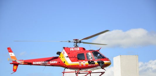 Helicóptero vermelho sobrevoa prédio com céu azul ao fundo