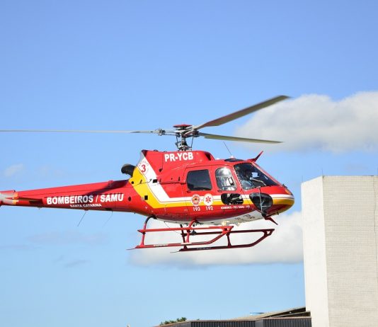Helicóptero vermelho sobrevoa prédio com céu azul ao fundo