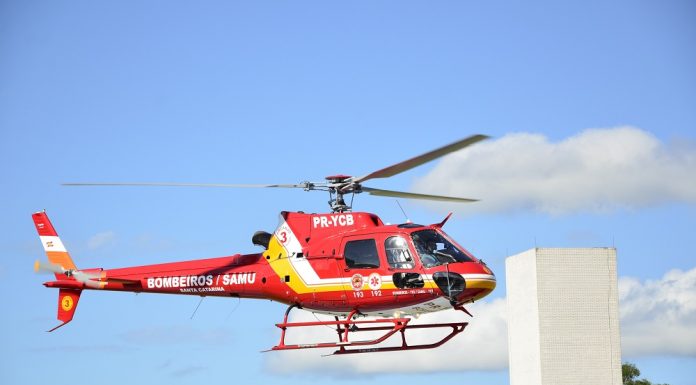 Helicóptero vermelho sobrevoa prédio com céu azul ao fundo