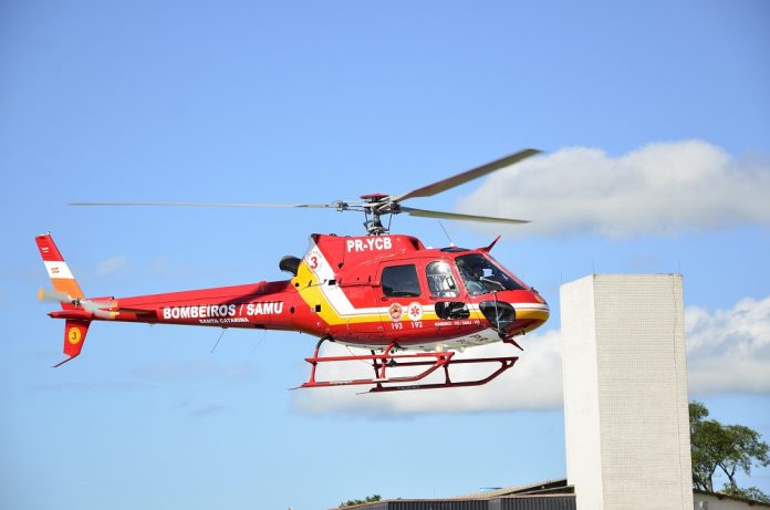 Helicóptero vermelho sobrevoa prédio com céu azul ao fundo