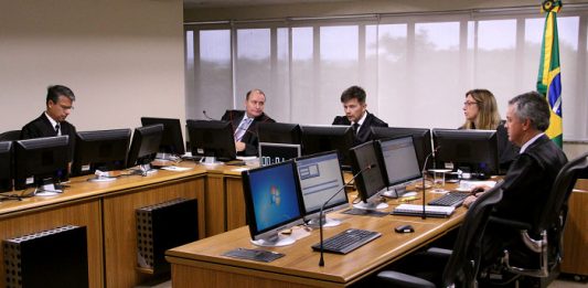 Bancada de juízes com computadores à frente em uma sala