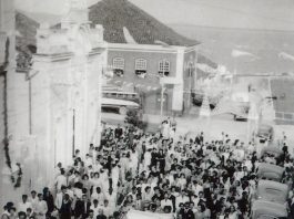 Grupo de pessoas visto de cima passa por uma rua de praça, em foto preto e branco