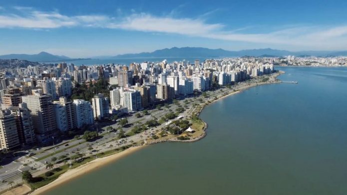 Vista aérea da avenida beira-mar norte, com os prédios ao longo, e o mar e céu azul num dia de sol