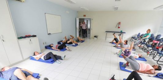 Pessoas deitadas no chão de uma sala praticam yoga em pequenos colchonetes