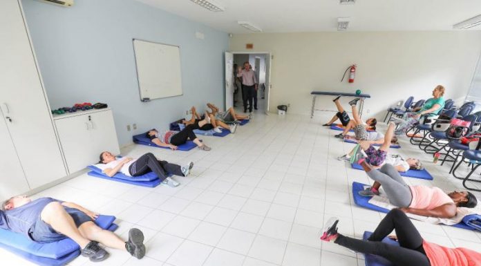 Pessoas deitadas no chão de uma sala praticam yoga em pequenos colchonetes