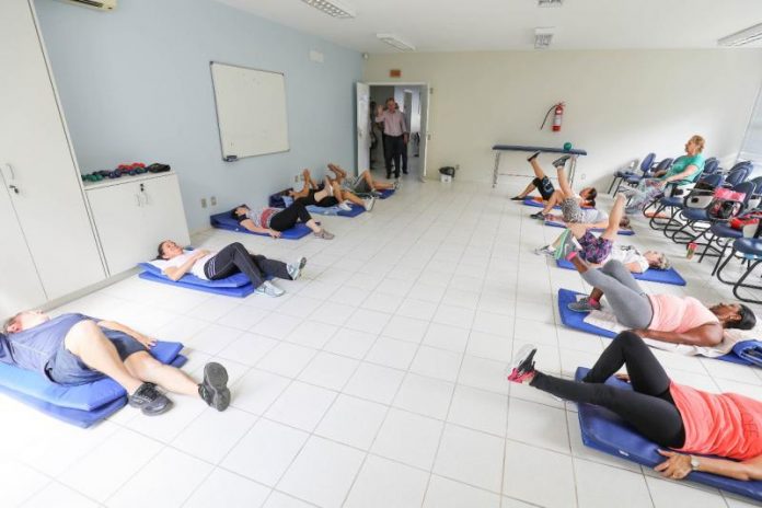 Pessoas deitadas no chão de uma sala praticam yoga em pequenos colchonetes