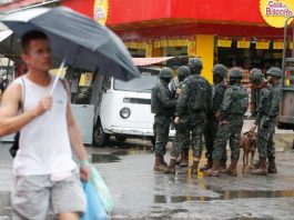 Temer vai destinar R$ 1 bilhão para intervenção no Rio Pedestre segurando guarda-chuva passa por soldados militares conversando em uma rua de comércios