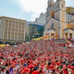 Multidão em frente à Catedral de Florianópolis vê Lula discursar, usando camiseta preta e boné vermelho do MST