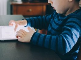 Luz de eletrônicos reduz em 88% melatonina de crianças Criança sentada em uma cadeira usa um tablet luminoso em cima de uma mesa