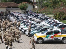 Batalhão de polícia militar anda em direção à dezenas de carros de polícia estacionados em um grande pátio para iniciar uma operação