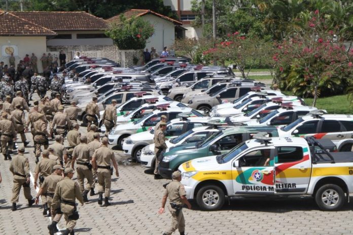 Batalhão de polícia militar anda em direção à dezenas de carros de polícia estacionados em um grande pátio para iniciar uma operação