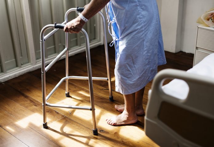 care-3031259_1280 Pessoa idosa de roupão de hospital se apoia em andador