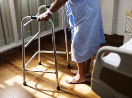 Pessoa idosa de roupão de hospital se apoia em andador