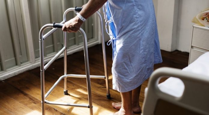 Pessoa idosa de roupão de hospital se apoia em andador