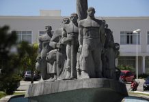 Monumento de pedra cinza em praça retratando imigrantes