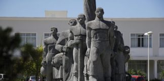 Monumento de pedra cinza em praça retratando imigrantes