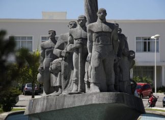 Monumento de pedra cinza em praça retratando imigrantes