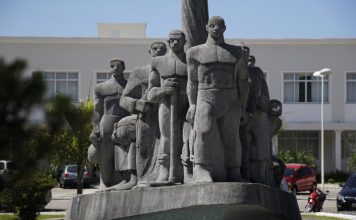 Monumento de pedra cinza em praça retratando imigrantes