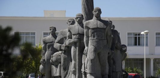 Monumento de pedra cinza em praça retratando imigrantes