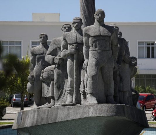 Monumento de pedra cinza em praça retratando imigrantes