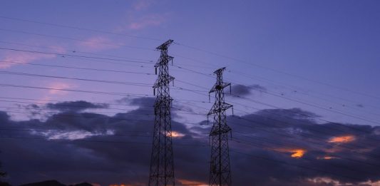 Imagem de duas torres de transmissão de energia elétrica com o por do sol ao fundo