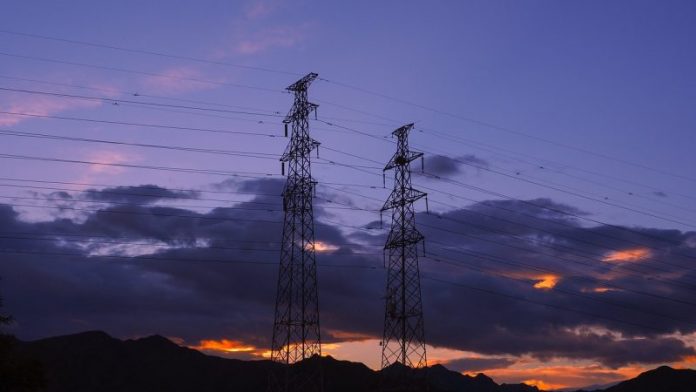 Imagem de duas torres de transmissão de energia elétrica com o por do sol ao fundo