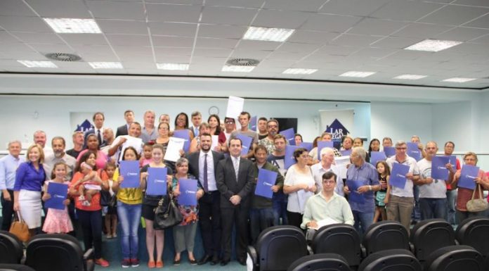 Dezenas de pessoas posam com certificados na frente de um auditório