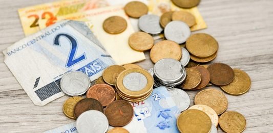 Plano Real completa 30 anos, com desvalorização de 87% Algumas notas de real e moedas espalhadas sobre a mesa