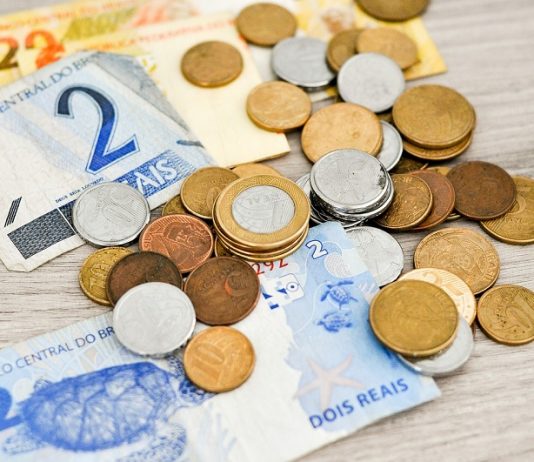 Algumas notas de real e moedas espalhadas sobre a mesa