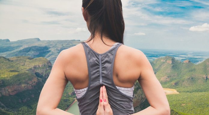 Imagem de uma mulher jovem de costas, com as mãos colocadas para trás em forma de oração; ao fundo, uma paisagem de montanhas