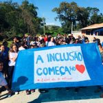 Com uma faixa à frente escrita "a inclusão começa no coração", alunos fazem passeata