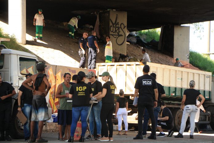 FOTO CAPA Foto em baixo do viaduto mostrando agentes de segurança na rua falando com usuários de drogas; ao fundo funcionários limpam e jogam lixo em caminhão