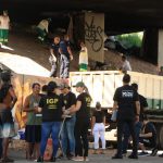 Foto em baixo do viaduto mostrando agentes de segurança na rua falando com usuários de drogas; ao fundo funcionários limpam e jogam lixo em caminhão