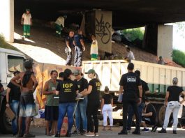 Investida contra a cracolândia da fronteira Florianópolis-SJ Foto em baixo do viaduto mostrando agentes de segurança na rua falando com usuários de drogas; ao fundo funcionários limpam e jogam lixo em caminhão