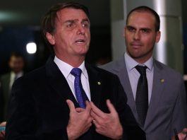 Dois homens de terno dão entrevista; um, à esquerda, gesticula; o outro (o filho) fica olhando