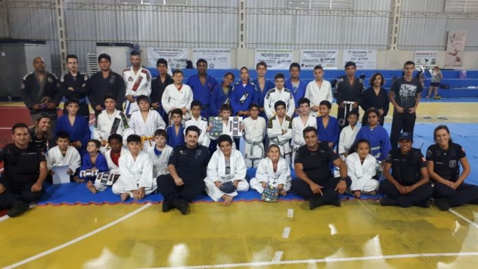 GMSJ quimono projeto jiu-jitsu sesc lisboa Grupo de pessoas posa para foto em uma quadra em ginásio, entre agentes de segurança e crianças de quimono