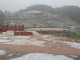 área rural coberta de granizo, terreno e rua em primeiro plano, morro ao fundo