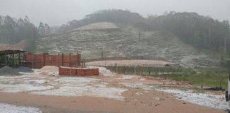 área rural coberta de granizo, terreno e rua em primeiro plano, morro ao fundo