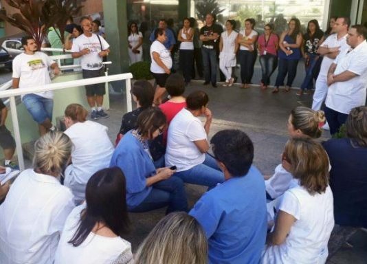 Pessoas sentadas na escadaria em frente ao hospital ouvem um homem falar em pé