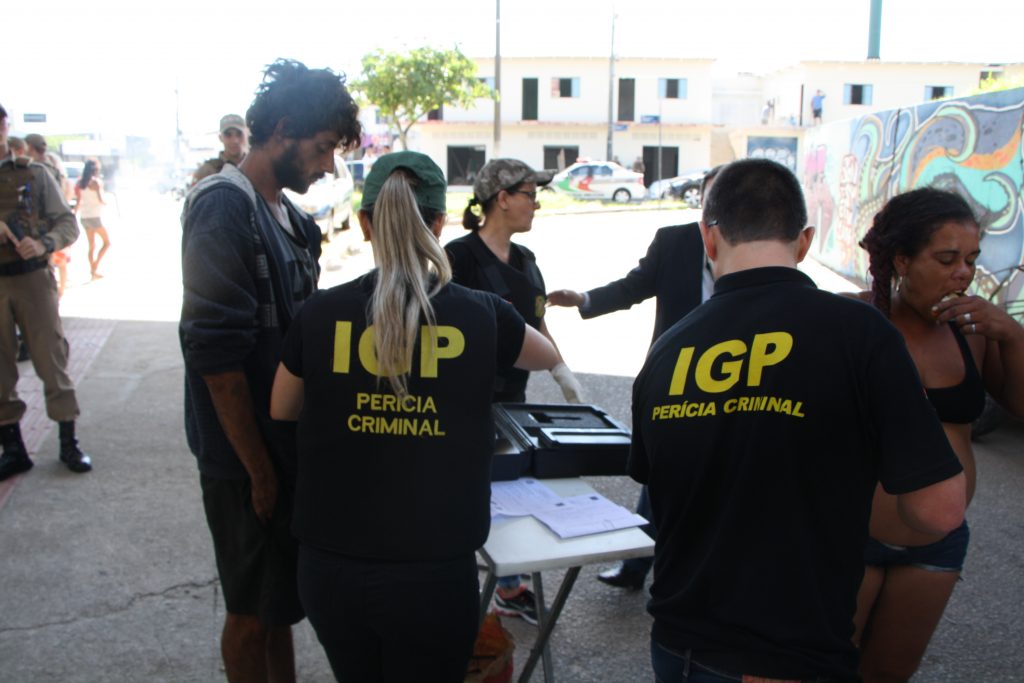 técnicos do igp de costas para a foto atendem moradores de rua em frente a uma pequena mesa sob o viaduto