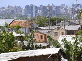 225 mil famílias em SC recebem o bolsa família Vista da cidade, com casas pobres em primeiro plano e prédio de classe alta ao fundo
