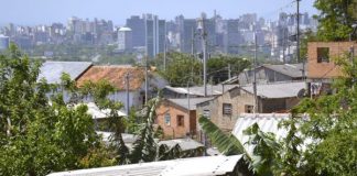 Vista da cidade, com casas pobres em primeiro plano e prédio de classe alta ao fundo