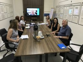 Grupo de oito pessoas em uma sala de reuniões, sentado em volta de uma mesa