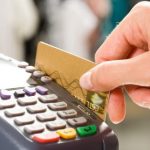 Close em uma mão segurando um cartão de crédito passando em um máquina de cartão