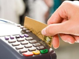 Close em uma mão segurando um cartão de crédito passando em um máquina de cartão