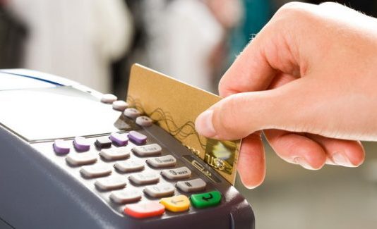 Close em uma mão segurando um cartão de crédito passando em um máquina de cartão