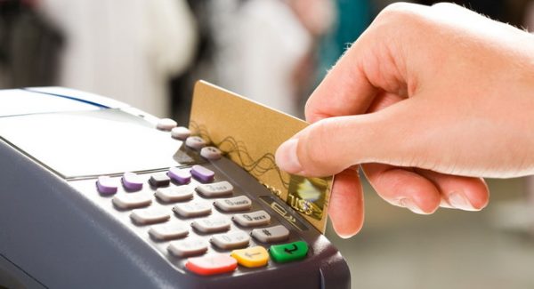Close em uma mão segurando um cartão de crédito passando em um máquina de cartão